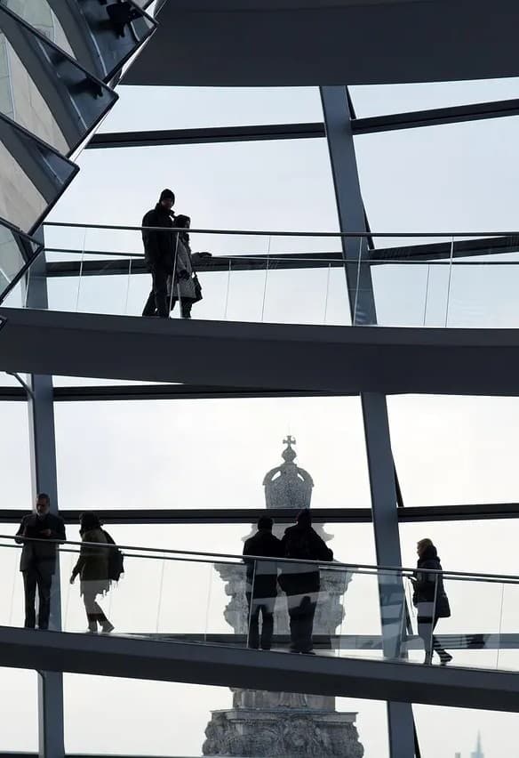 Siluetas de personas caminando por una rampa curva dentro de una moderna cúpula de vidrio